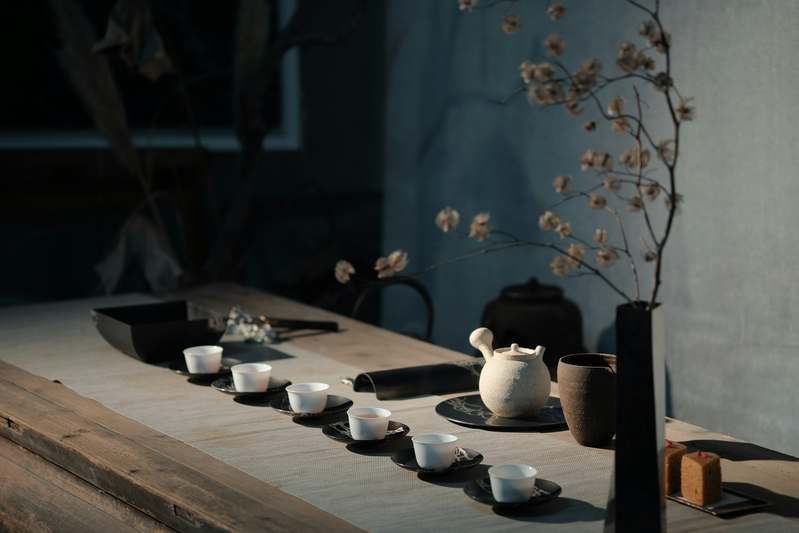 Close-up of a stainless steel chain-and-ball tea infuser resting on a rustic wooden countertop beside a ceramic mug and loose-leaf green tea