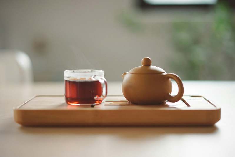 Overhead photo of multiple tea infusers — ball, basket, spoon, and collapsible silicone — arranged neatly on a gray workshop-style mat with calipers and a notebook